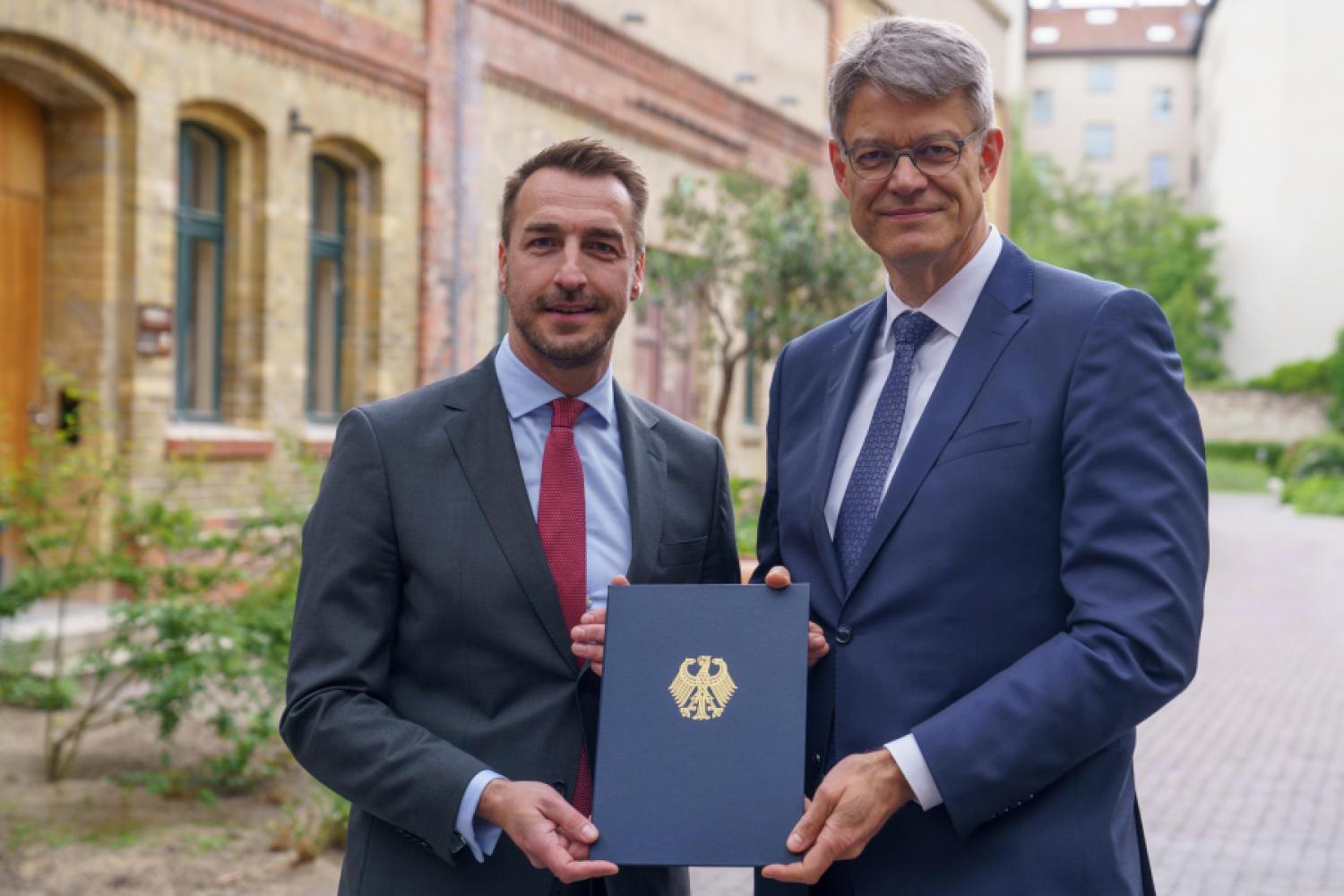 From the hands of Dr. Patrick Schnieder, Federal Minister for Transport (right), Steffen Bauer, CEO of HGK Shipping, received permission for his company to conduct test operations of remotely controlled inland vessels in the German canal network. (Image: Stella Scheibenzuber | HGK Shipping)